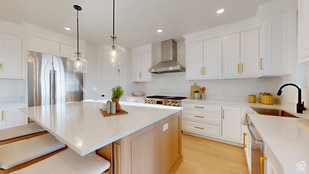 Kitchen featuring wall chimney range hood, a center island, a kitchen bar, light wood-style floors, and white cabinets