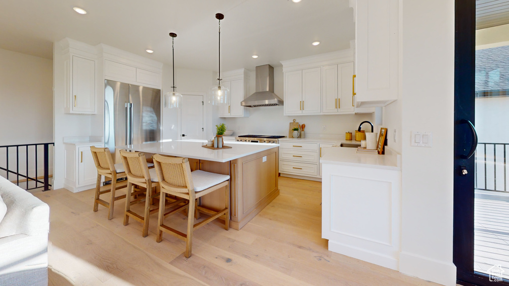 Kitchen featuring wall chimney range hood, light wood-type flooring, a kitchen island, white cabinetry, and light countertops