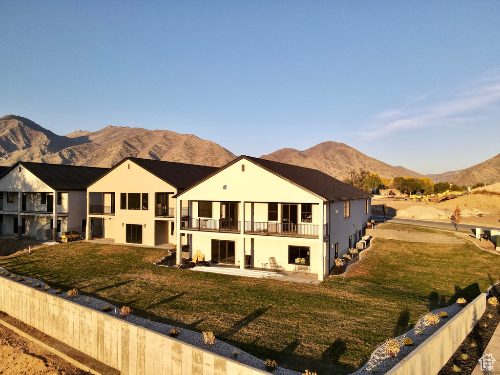 View of front of house with a balcony, a patio area, a mountain view, and a front lawn