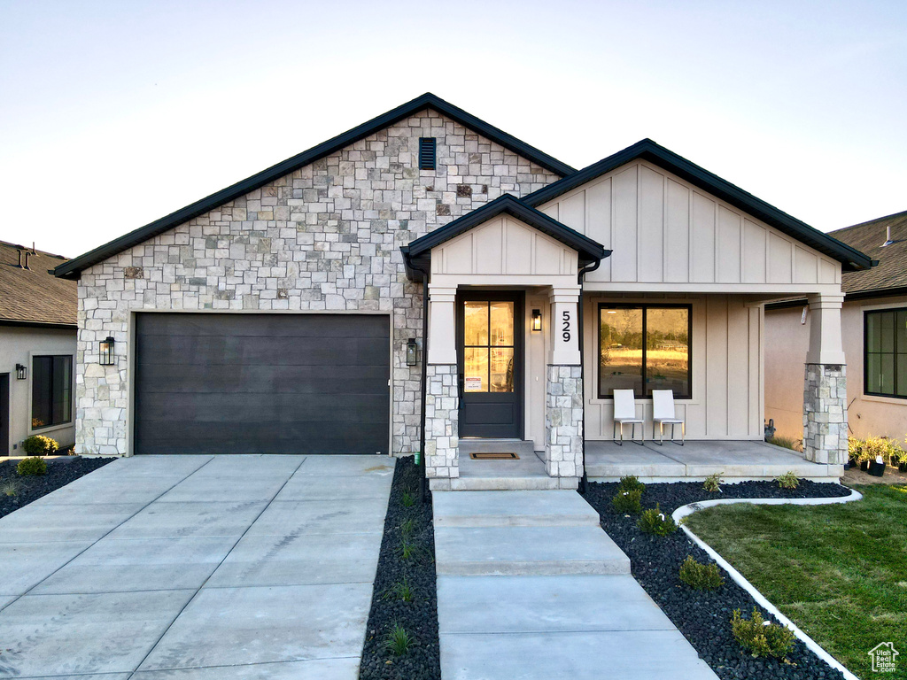 View of front facade with board and batten siding, a garage, driveway, and stone siding