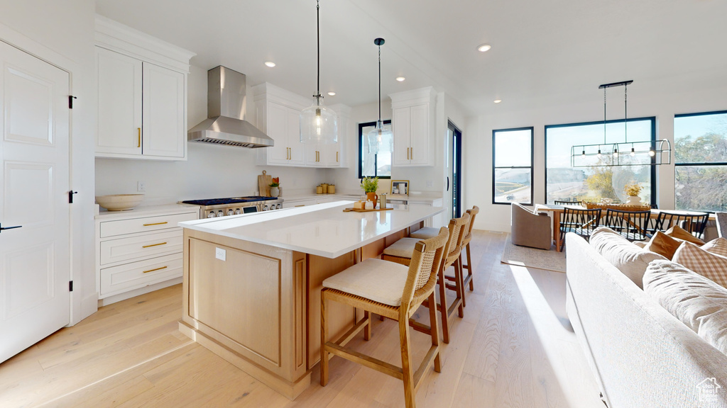 Kitchen with wall chimney exhaust hood, light wood finished floors, light countertops, a center island, and recessed lighting