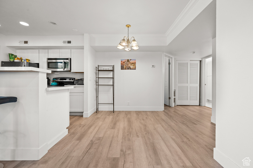 Kitchen featuring appliances with stainless steel finishes, light wood finished floors, white cabinets, crown molding, and a chandelier