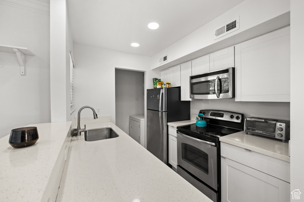 Kitchen with stainless steel appliances, white cabinetry, light stone countertops, recessed lighting, and washer / dryer