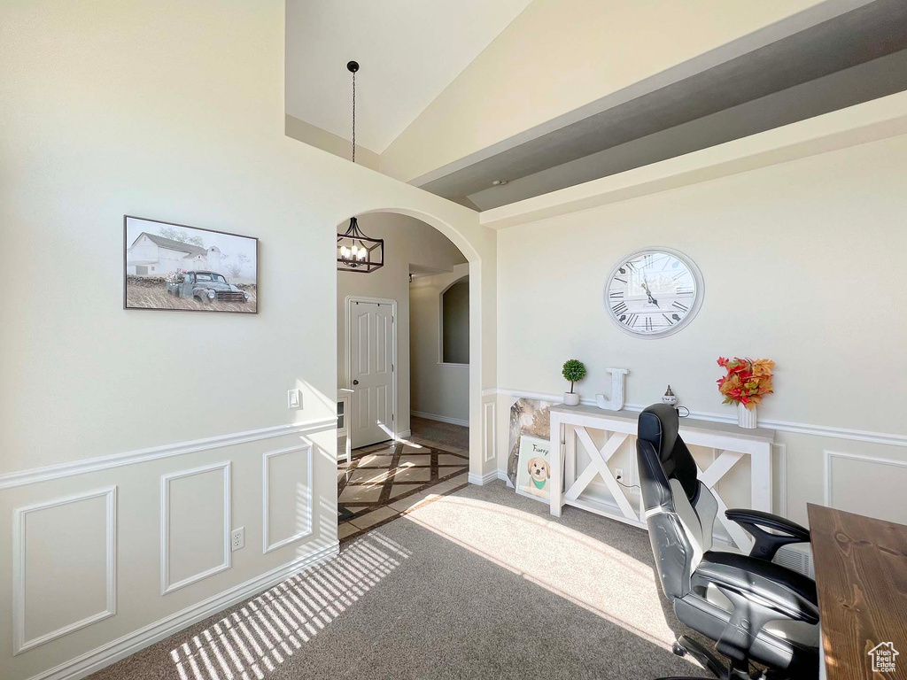 Carpeted office space featuring arched walkways, wainscoting, a decorative wall, and lofted ceiling