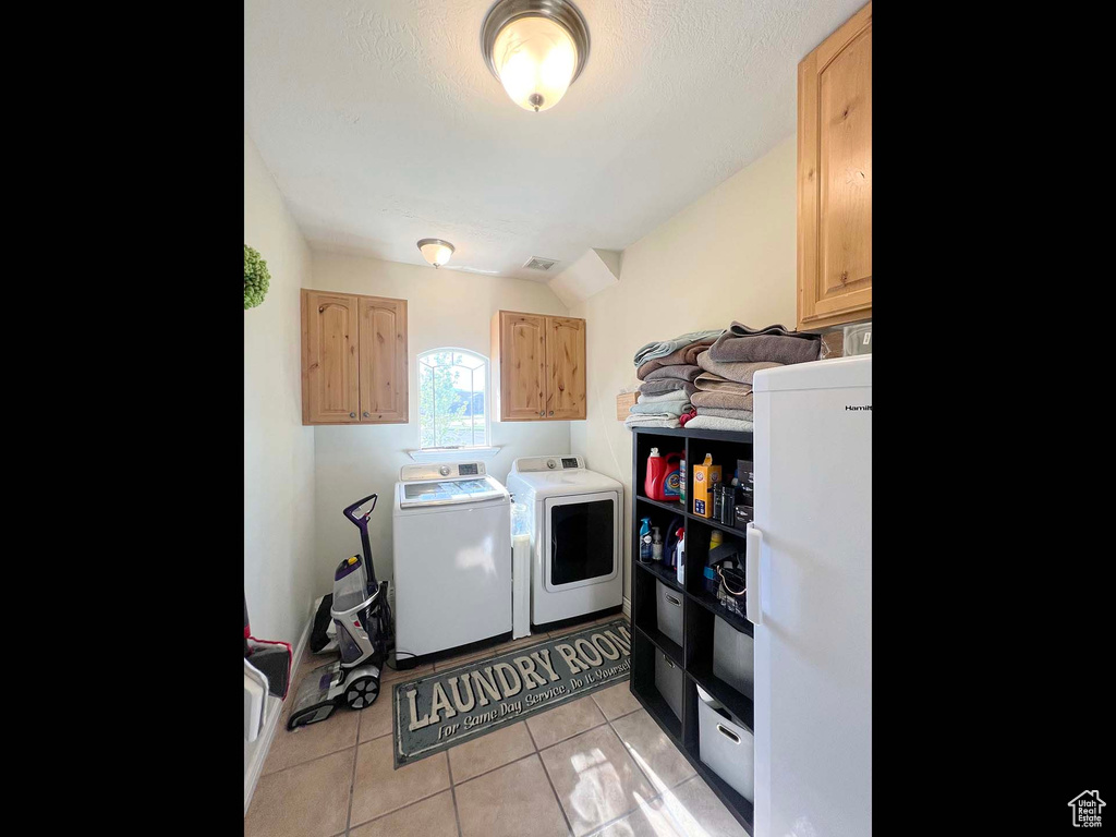 Laundry area featuring washer and dryer, cabinet space, and light tile patterned floors
