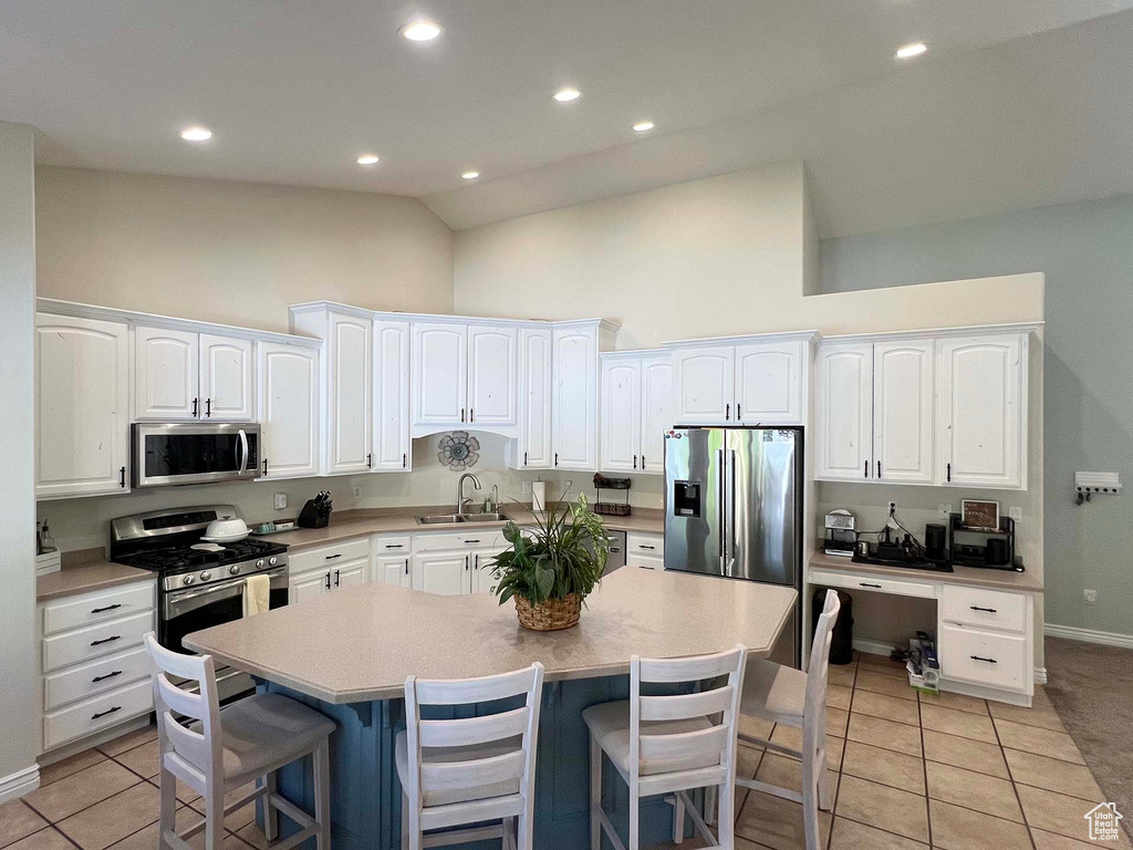 Kitchen with stainless steel appliances, high vaulted ceiling, white cabinetry, a kitchen breakfast bar, and a center island