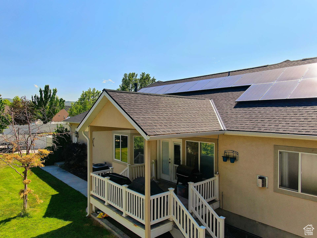 Rear view of property featuring roof with shingles, roof mounted solar panels, a yard, stucco siding, and french doors
