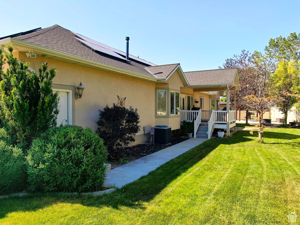 Rear view of house featuring stucco siding, solar panels, a lawn, and a shingled roof