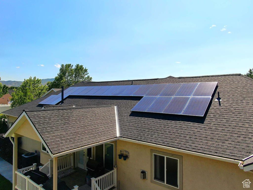 View of side of home with a shingled roof, stucco siding, and solar panels
