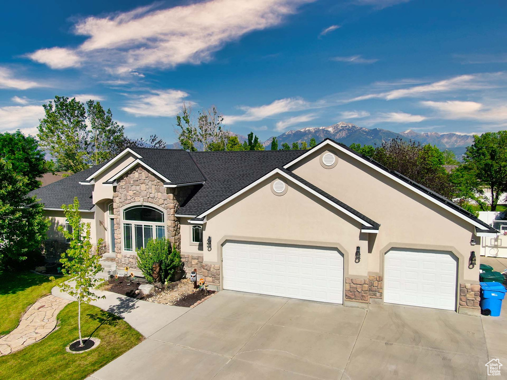 View of front facade with stone siding, driveway, stucco siding, a garage, and a mountain view