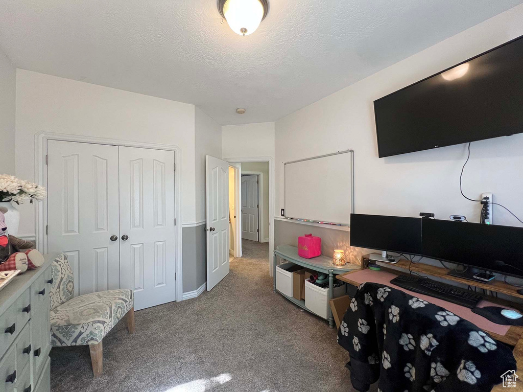 Carpeted bedroom with a closet, a textured ceiling, and a desk
