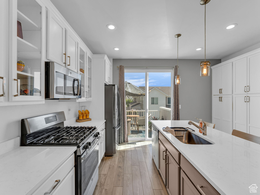 Kitchen with stainless steel appliances, recessed lighting, light wood finished floors, glass insert cabinets, and white cabinetry