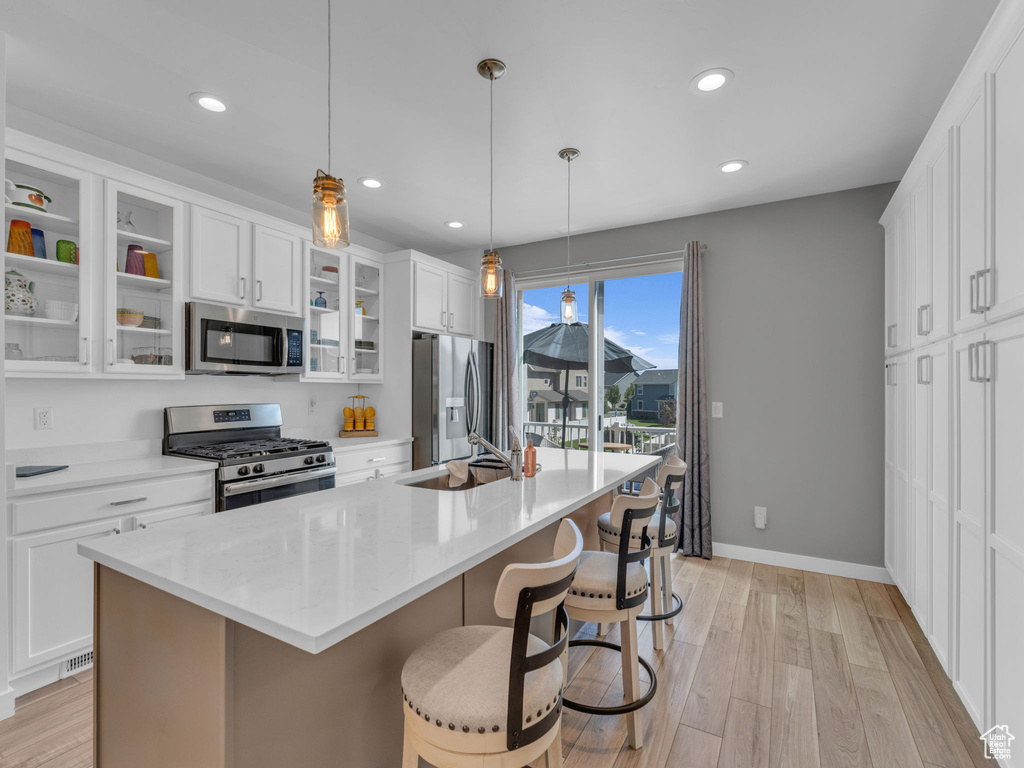 Kitchen with stainless steel appliances, an island with sink, a kitchen bar, recessed lighting, and white cabinetry
