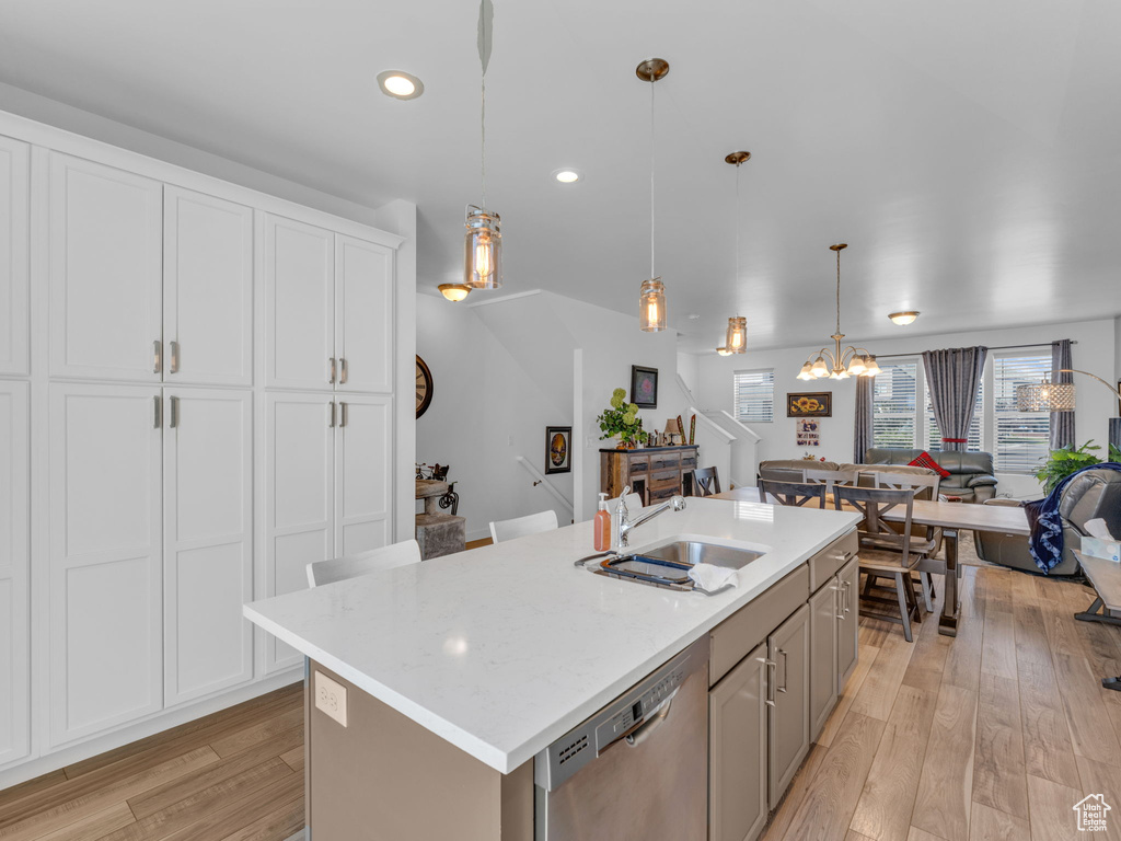 Kitchen with stainless steel dishwasher, a chandelier, open floor plan, an island with sink, and light wood finished floors