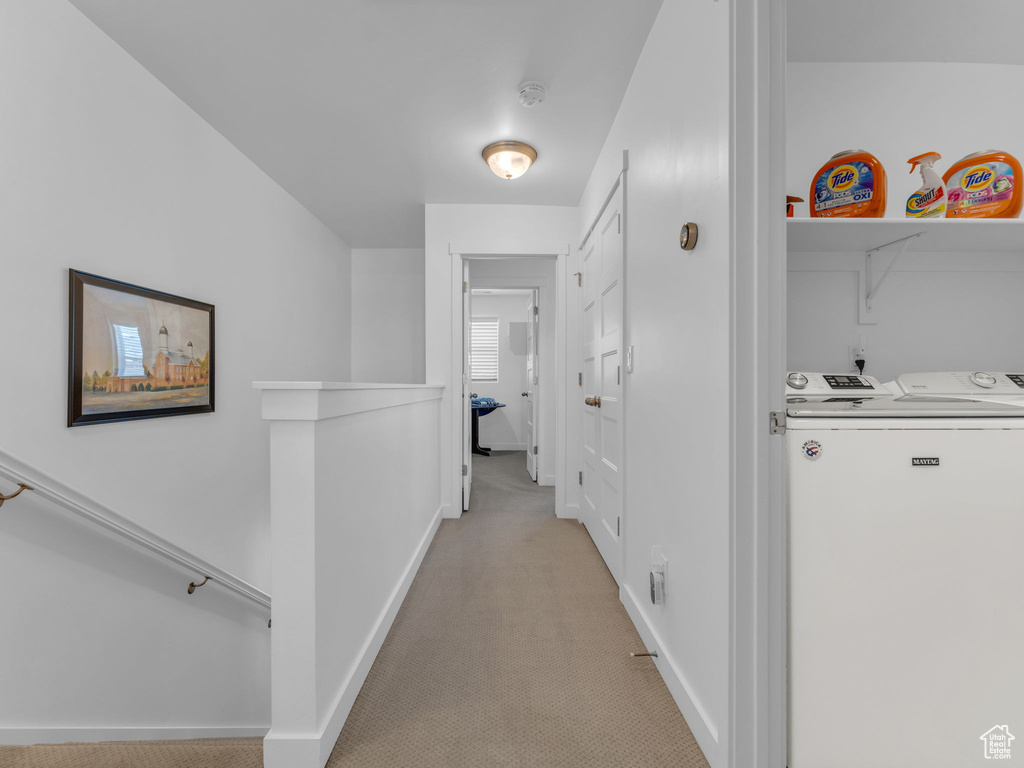 Hall with light colored carpet, washer and clothes dryer, and an upstairs landing