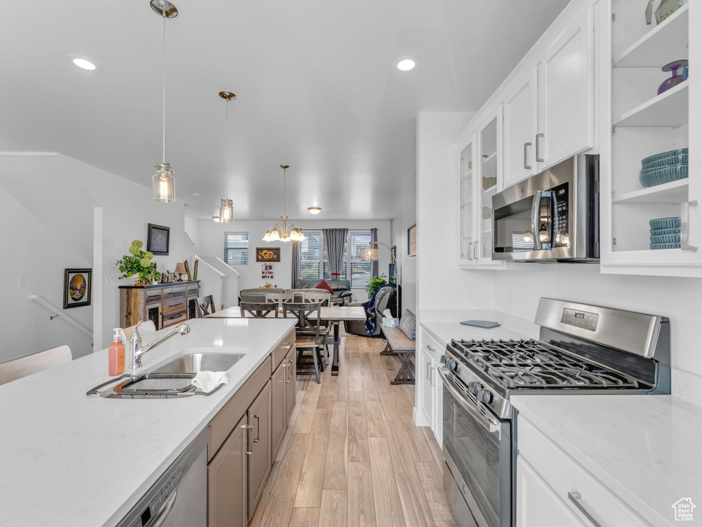 Kitchen featuring appliances with stainless steel finishes, light wood finished floors, glass insert cabinets, hanging light fixtures, and white cabinetry