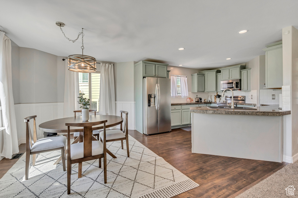 Kitchen featuring appliances with stainless steel finishes, green cabinetry, healthy amount of natural light, a wainscoted wall, and dark wood-type flooring