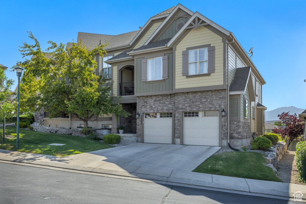 View of front of house with stone siding, driveway, a front lawn, a garage, and a balcony