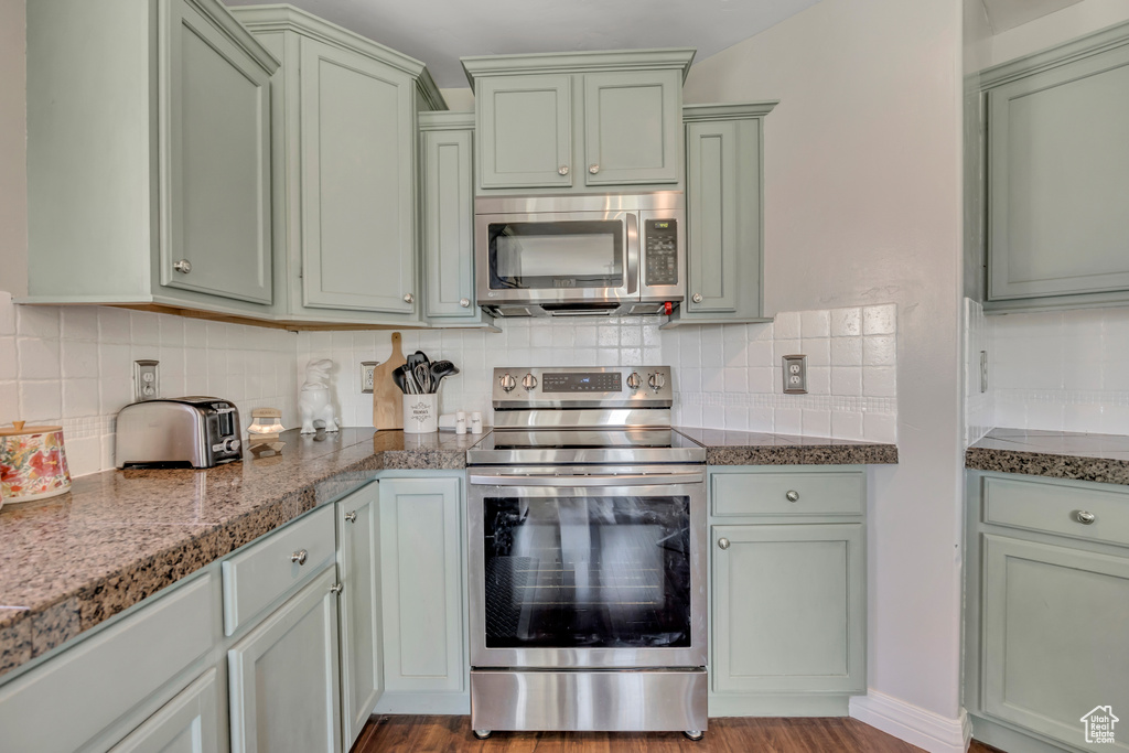 Kitchen with appliances with stainless steel finishes, green cabinets, and tasteful backsplash