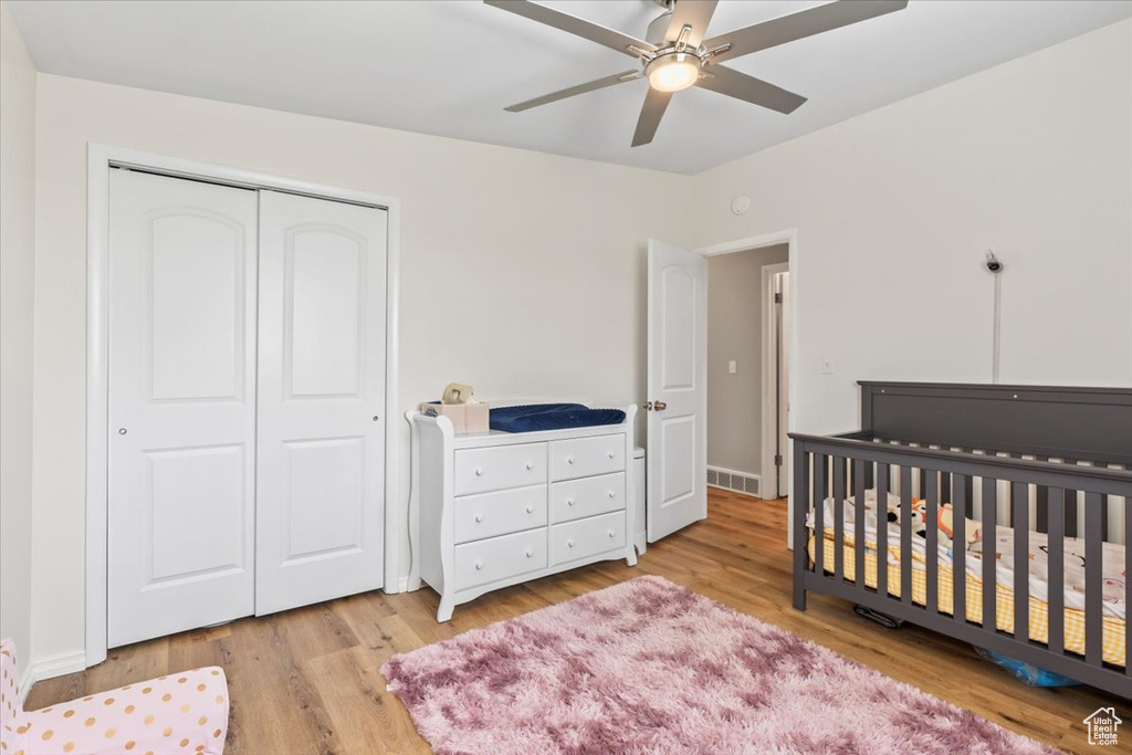 Bedroom with a closet, light wood finished floors, a nursery area, and ceiling fan
