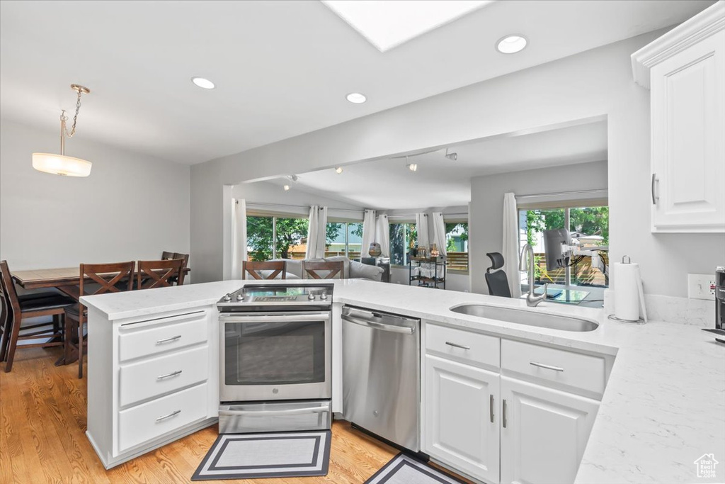 Kitchen with stainless steel appliances, a peninsula, white cabinets, light wood-style flooring, and recessed lighting