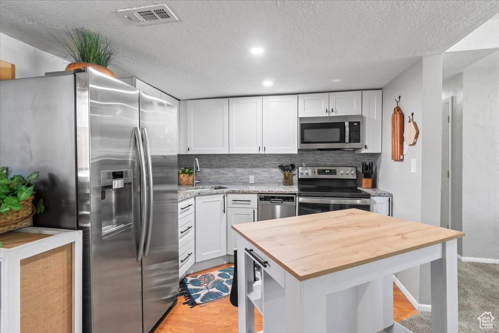 Kitchen featuring stainless steel appliances, wood counters, white cabinetry, a textured ceiling, and tasteful backsplash