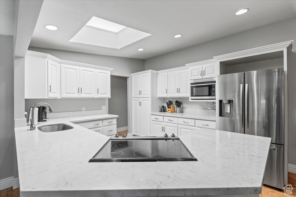Kitchen featuring stainless steel appliances, a skylight, white cabinets, recessed lighting, and light stone countertops
