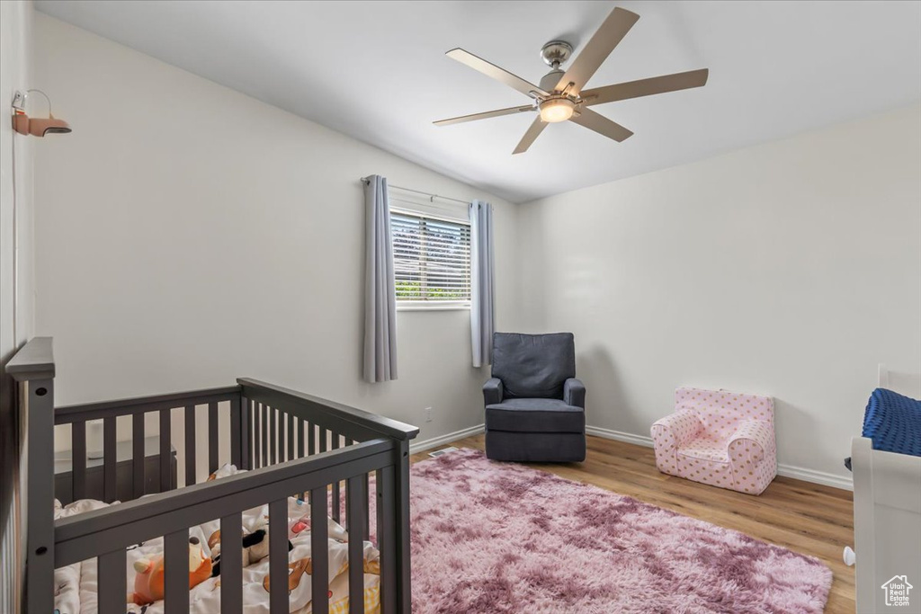 Bedroom featuring a crib, wood finished floors, lofted ceiling, and a ceiling fan
