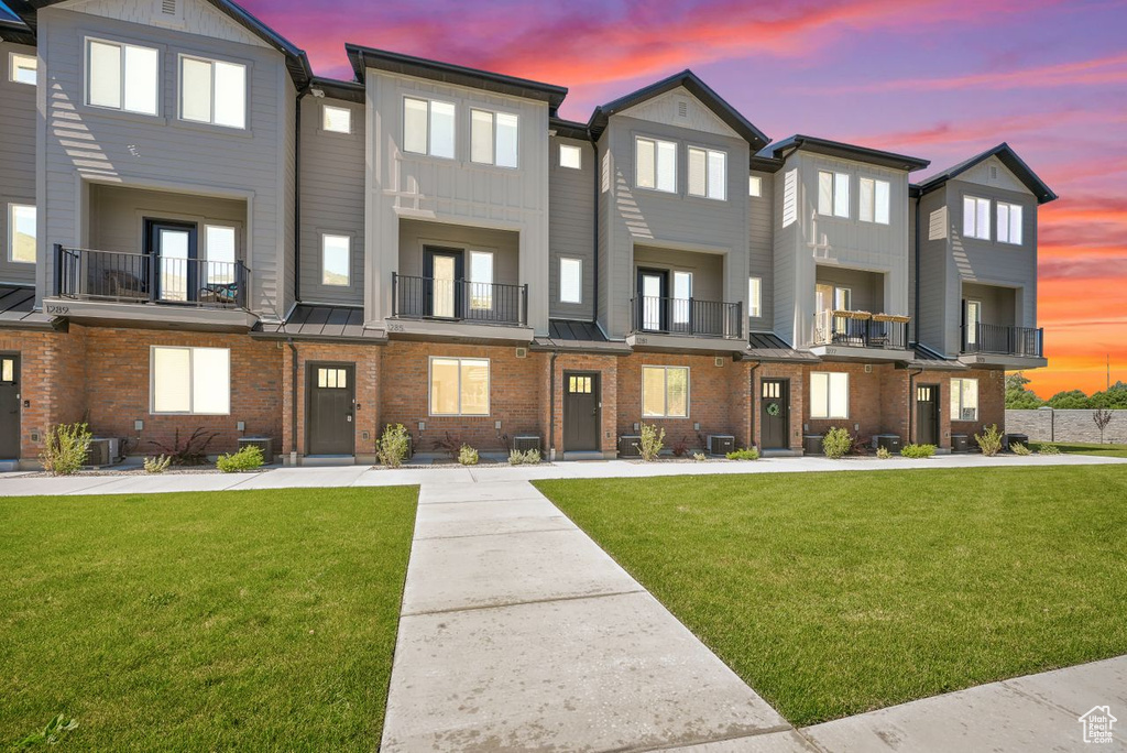 Townhome / multi-family property with a front lawn, brick siding, a standing seam roof, and board and batten siding