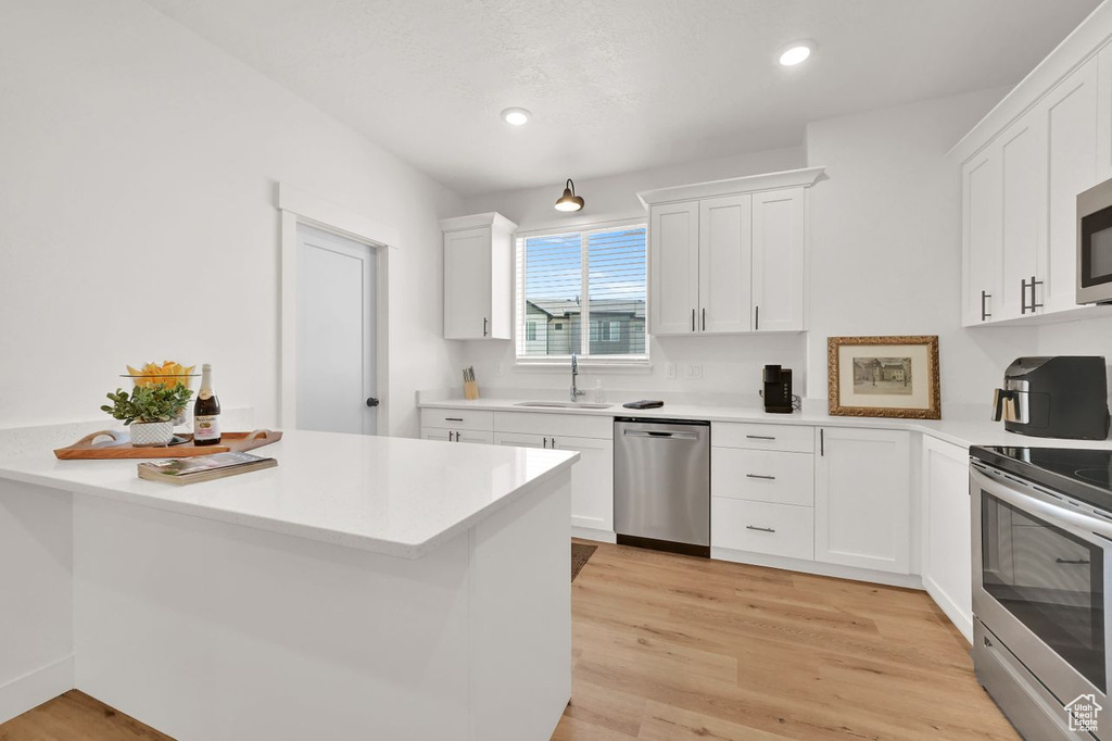 Kitchen with appliances with stainless steel finishes, white cabinets, light countertops, light wood-type flooring, and recessed lighting