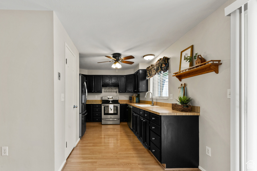 Kitchen with appliances with stainless steel finishes, dark cabinetry, ceiling fan, light wood finished floors, and light countertops
