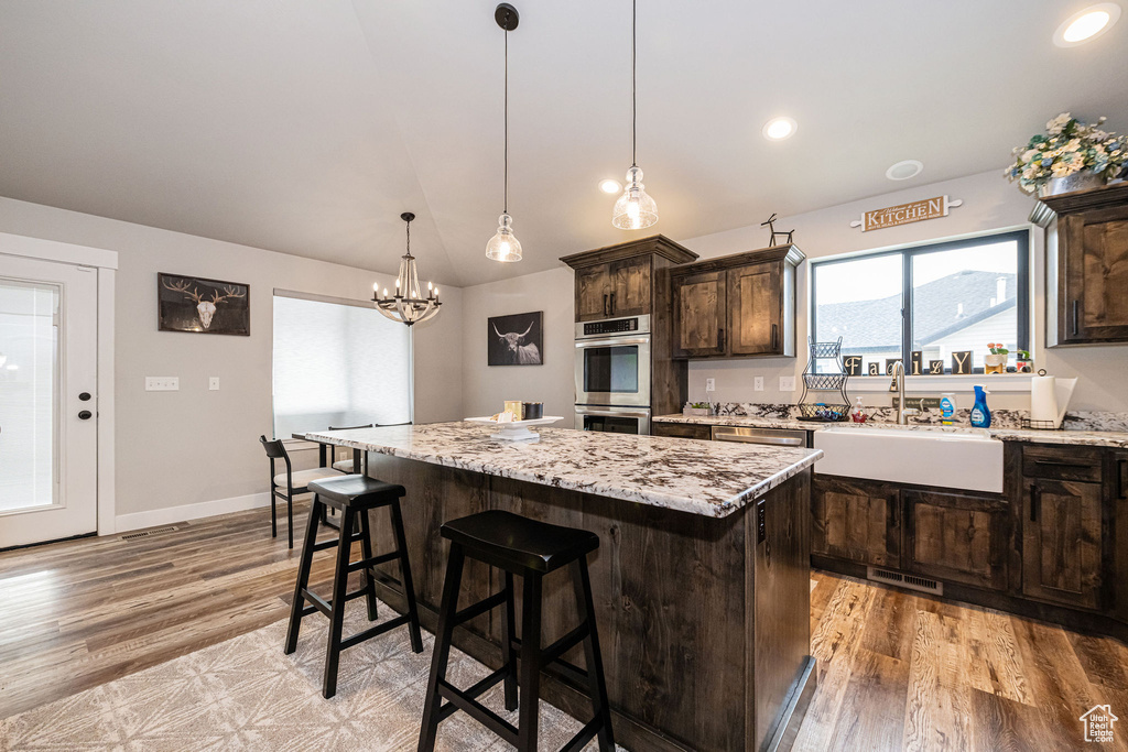 Kitchen with double oven, light wood-style flooring, dark brown cabinets, a center island, and recessed lighting