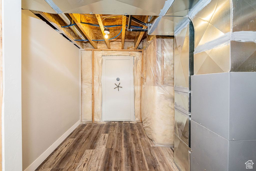 Unfinished basement featuring heating unit and wood finished floors