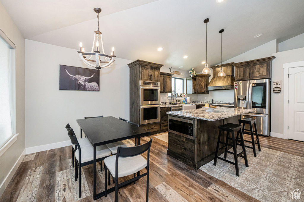 Kitchen featuring stainless steel appliances, lofted ceiling, a chandelier, dark brown cabinetry, and wood finished floors