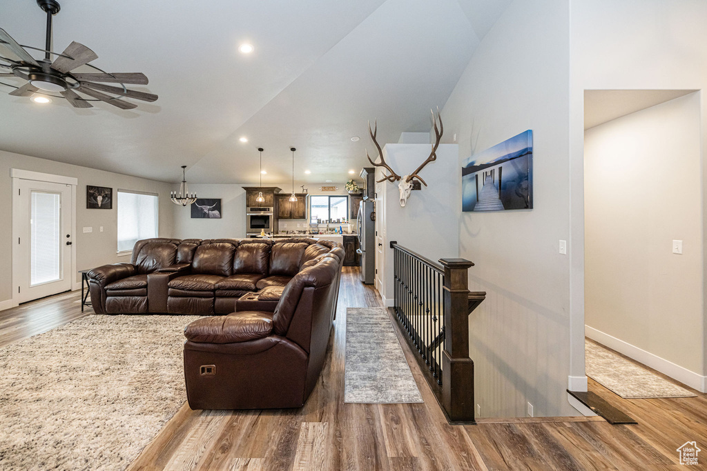 Living room featuring wood finished floors, a chandelier, a ceiling fan, vaulted ceiling, and recessed lighting