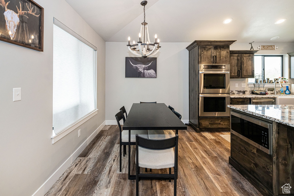 Kitchen with stainless steel appliances, a chandelier, dark brown cabinetry, dark wood-type flooring, and vaulted ceiling