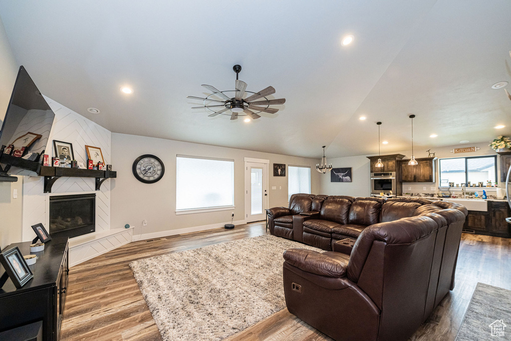 Living room featuring a ceiling fan, a tiled fireplace, wood finished floors, lofted ceiling, and recessed lighting