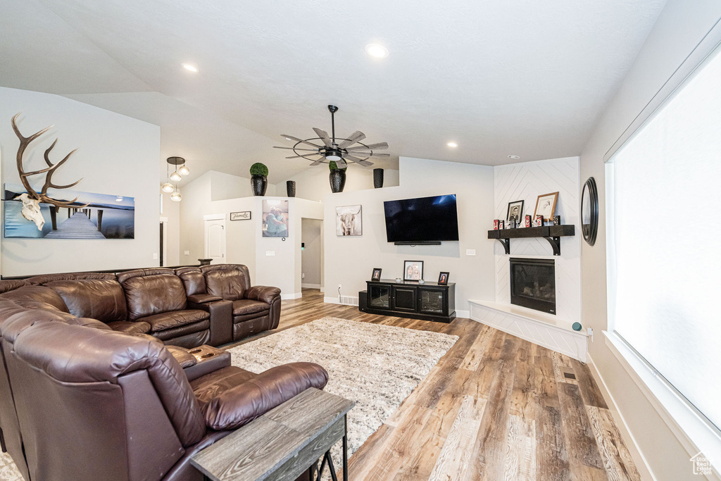 Living area featuring lofted ceiling, wood finished floors, a ceiling fan, a large fireplace, and recessed lighting