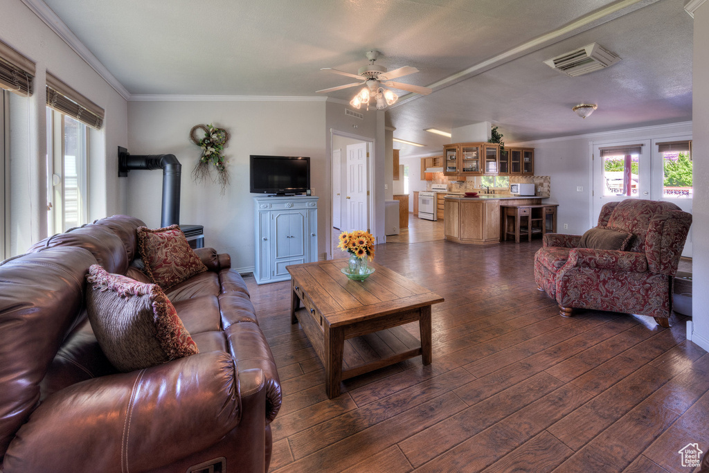 Living area featuring a wood stove, crown molding, dark wood-style floors, and a ceiling fan