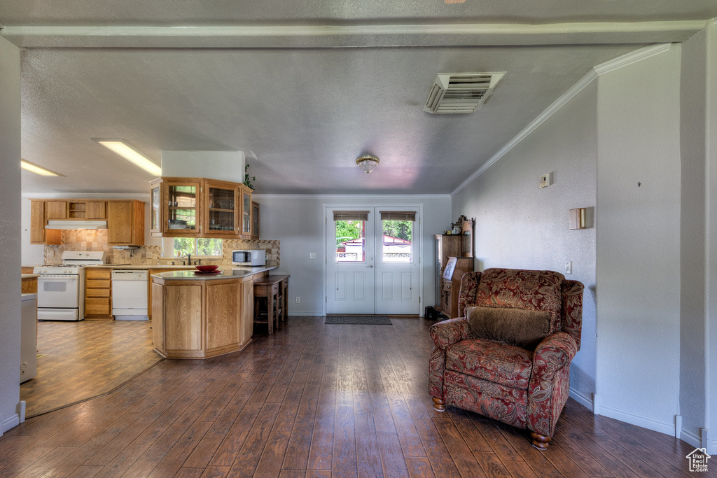 Kitchen featuring white appliances, open floor plan, ornamental molding, light countertops, and glass insert cabinets