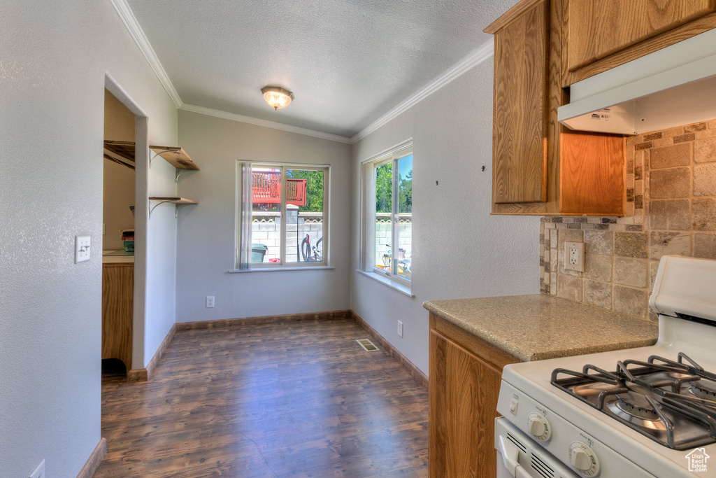 Kitchen with white range with gas stovetop, under cabinet range hood, brown cabinetry, crown molding, and dark wood-style flooring