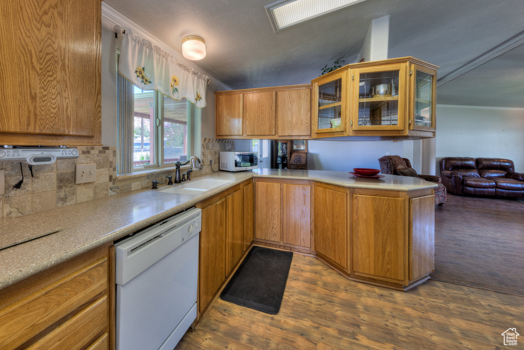 Kitchen with white dishwasher, stainless steel microwave, decorative backsplash, light countertops, and dark wood-type flooring
