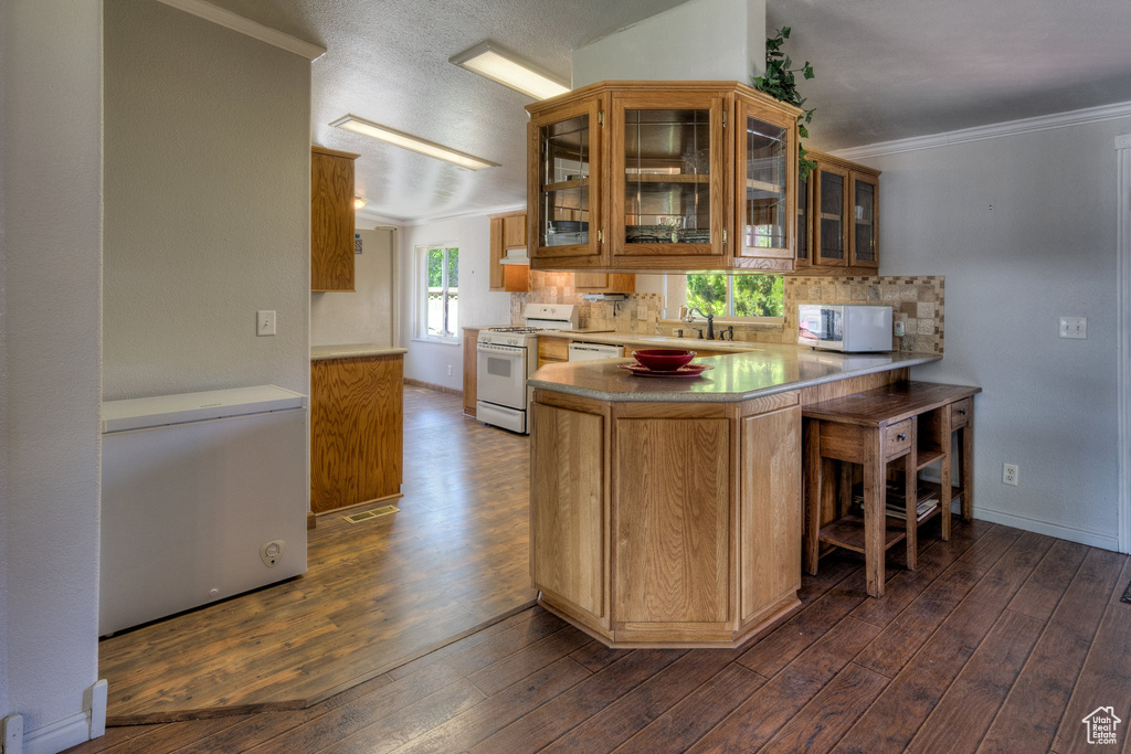 Kitchen featuring white appliances, dark wood finished floors, tasteful backsplash, crown molding, and glass insert cabinets