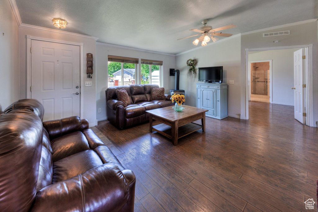 Living room with dark wood finished floors, ornamental molding, ceiling fan, and a wood stove