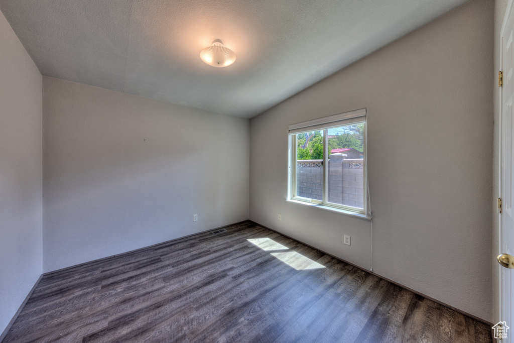 Empty room with dark wood finished floors and vaulted ceiling