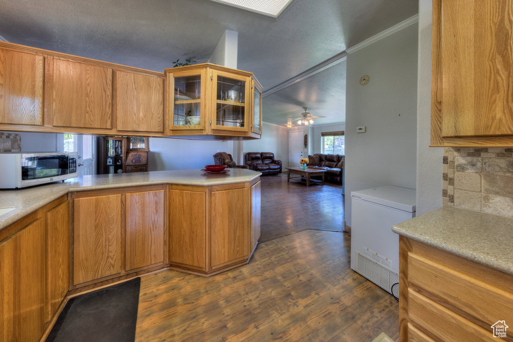 Kitchen featuring stainless steel microwave, refrigerator, light countertops, glass insert cabinets, and crown molding
