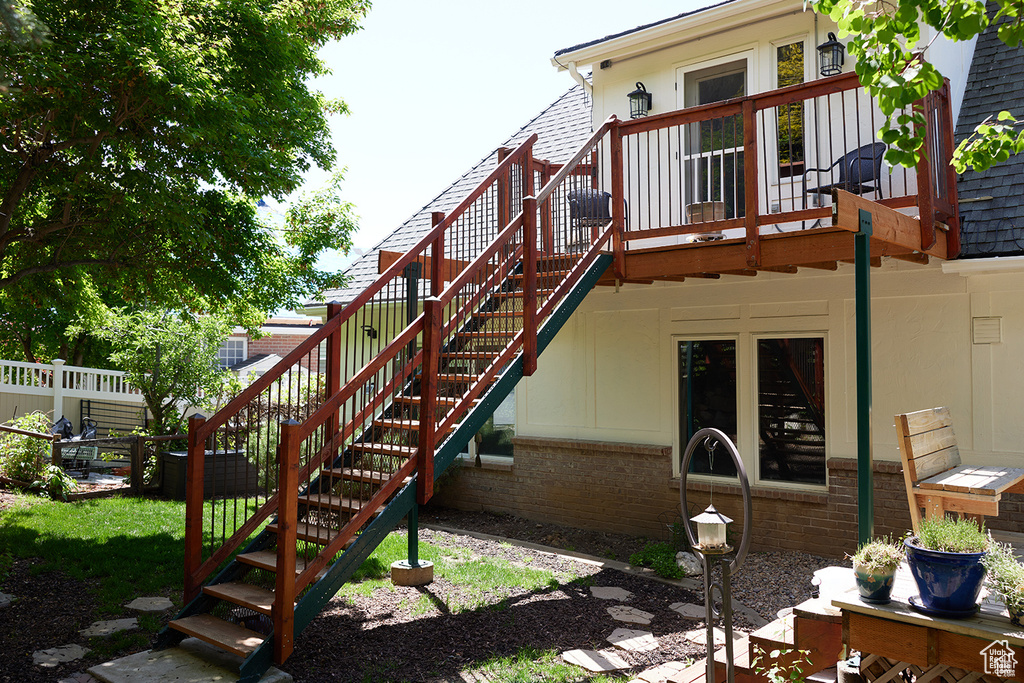 Rear view of house featuring stairs, brick siding, a wooden deck, and roof with shingles