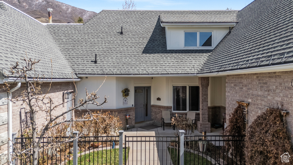 View of front of home featuring a shingled roof, a patio, brick siding, and stucco siding