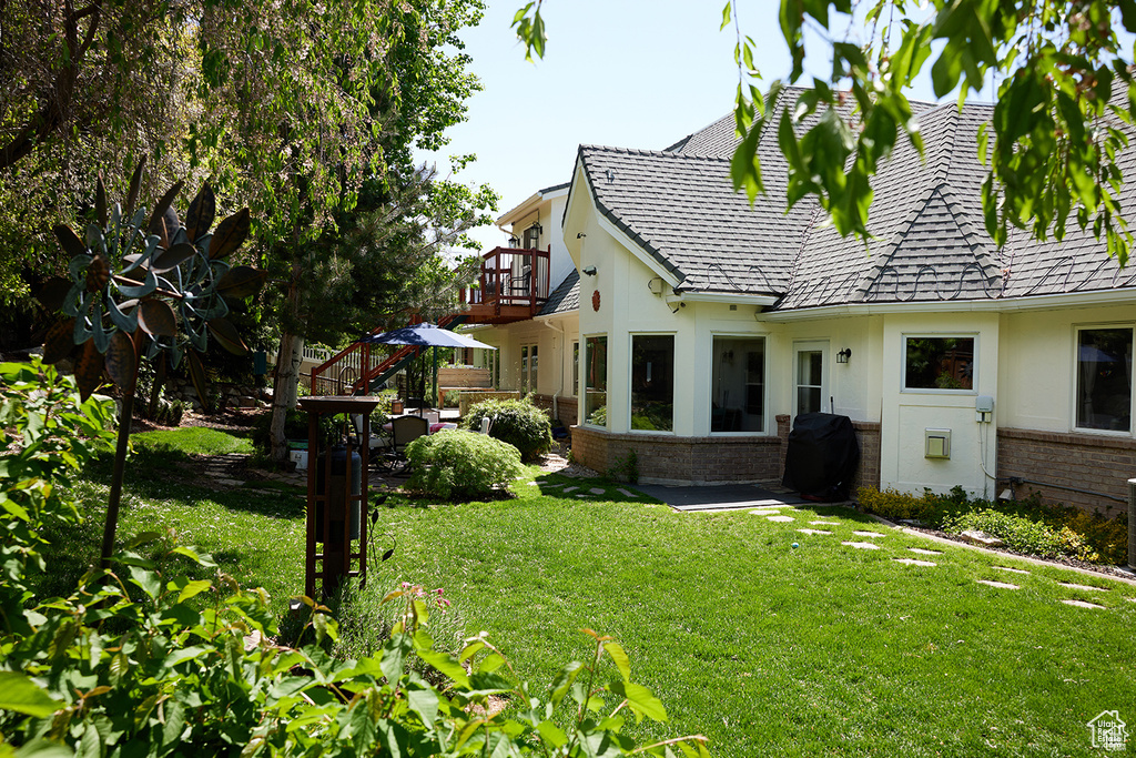 View of side of property featuring brick siding, a yard, a balcony, a chimney, and stucco siding