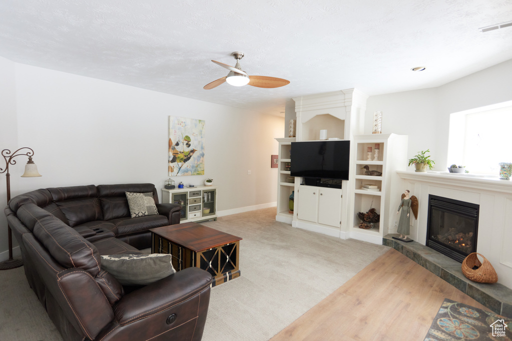 Living room with ceiling fan, a tiled fireplace, and wood finished floors